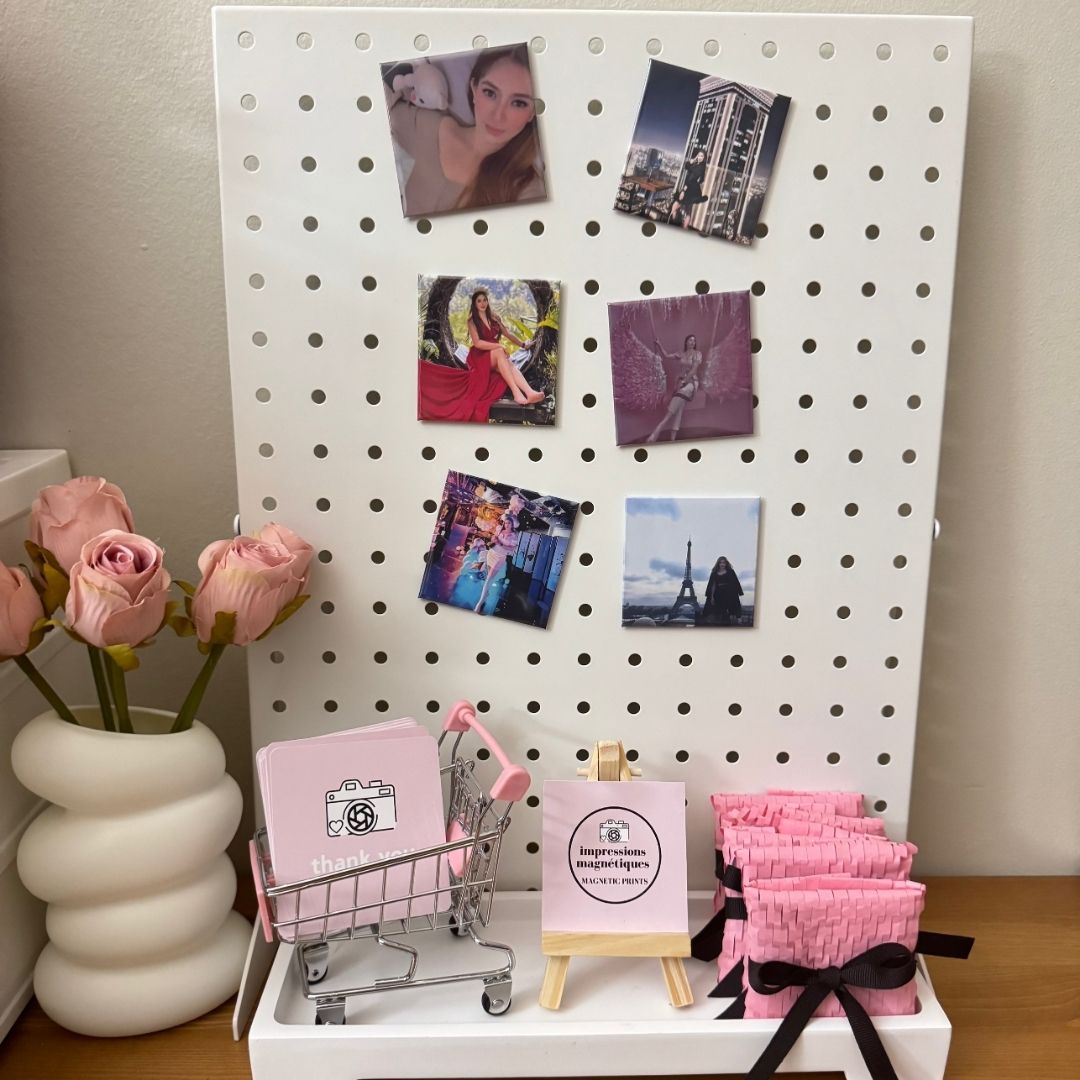 White pegboard with square custom photo magnet, a mini cart with pink thank-you cards, a small easel, and pink gift display.