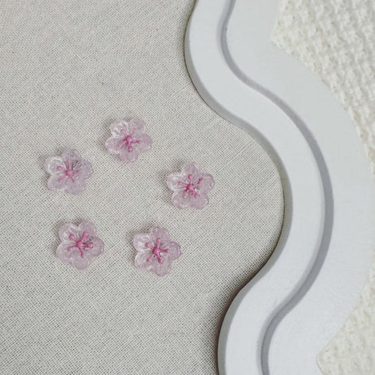 Five translucent pink cherry blossom-shaped magnets with glitter details on a fabric-covered board with a decorative white frame.