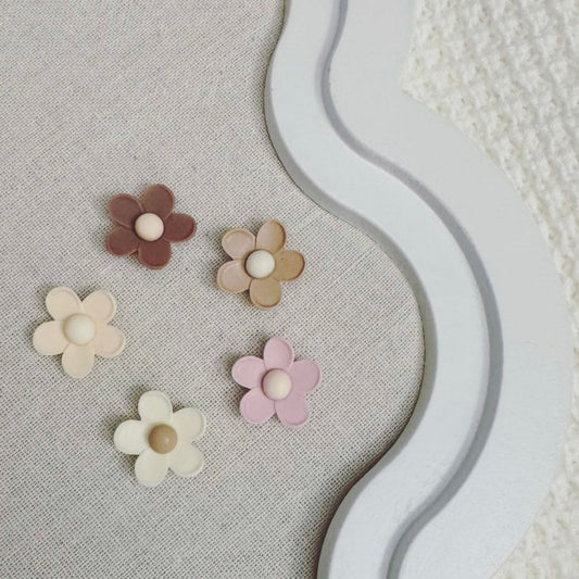 Five pastel and neutral-toned flower-shaped magnets on a fabric-covered board with a decorative white frame.