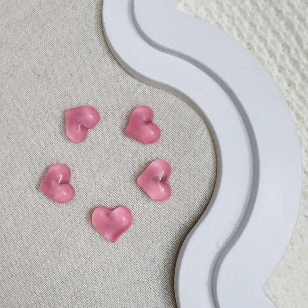 Five pink translucent heart-shaped magnets arranged in a circle on a fabric-covered board with a decorative white frame.