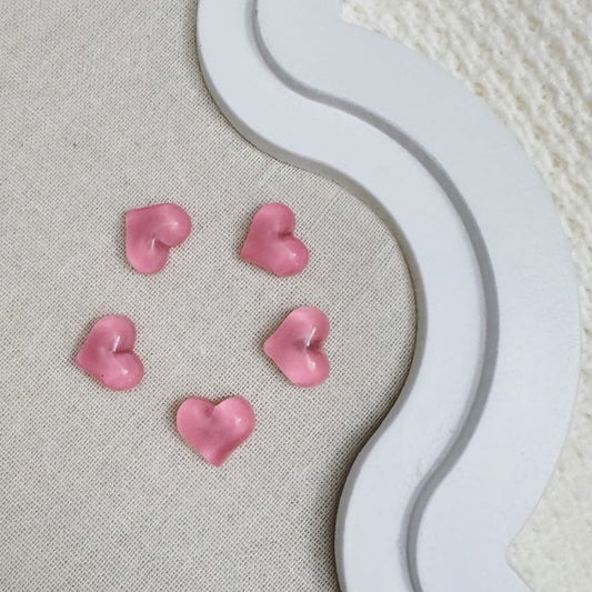 Five pink translucent heart-shaped magnets arranged in a circle on a fabric-covered board with a decorative white frame.