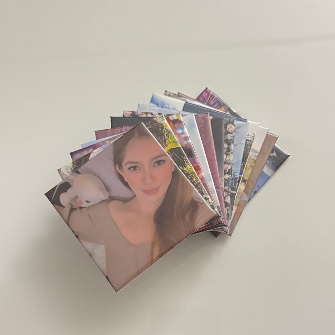 A stack of 12 square custom photo magnets fanned out on a white surface, featuring a portrait of a woman holding a plush toy on top.